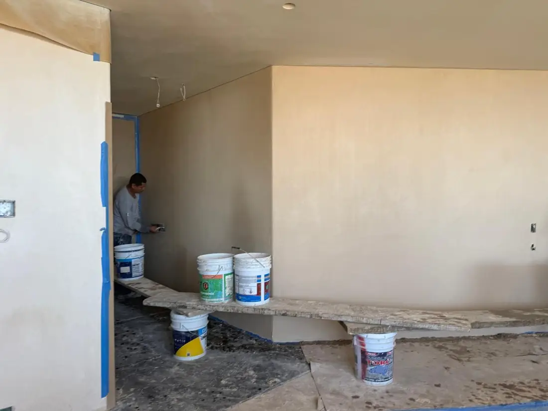 An ArquiVal applicator spreading chukum with a trowel on an interior wall, protective tape still on the edges