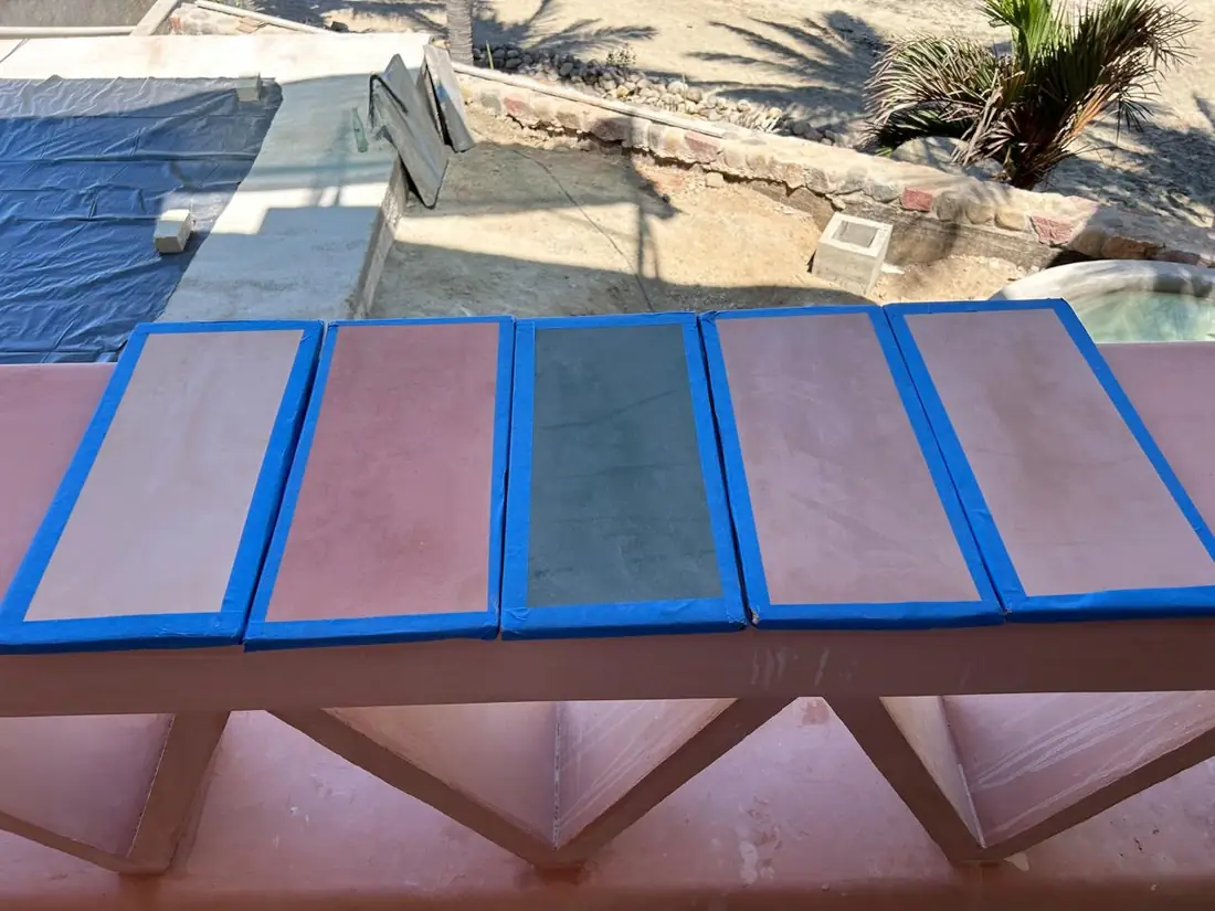 Cinco muestras de color de acabado, enmarcadas con cinta y secando al sol sobre el pretil de una obra