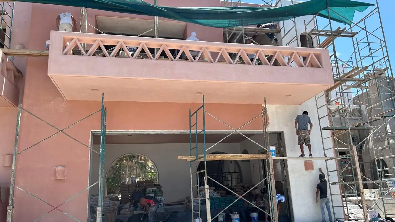 Cuadrilla aplicando acabado y pintura sobre la fachada de un edificio, con andamio montado en los dos niveles y malla de protección