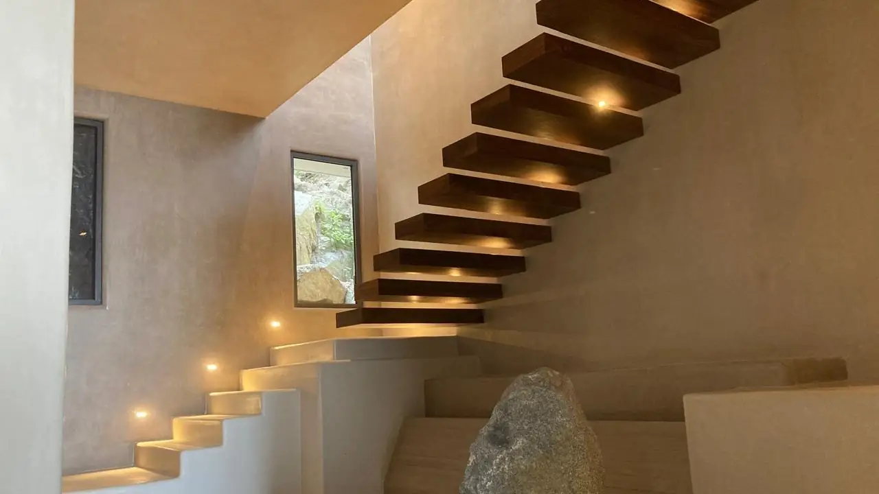 Cantilevered wooden stair treads over a seamless microcement floor and base, with polished stucco walls and recessed grazing light at every tread